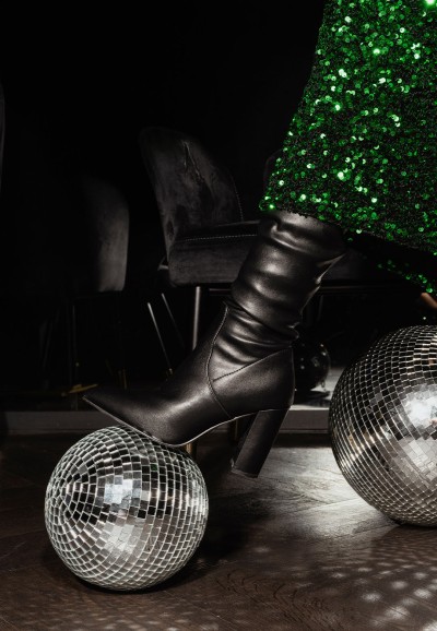 Nahaufnahme des Models mit glänzendem grünen Rock und schwarzen Lauren Stiefeln zwischen Discokugeln.