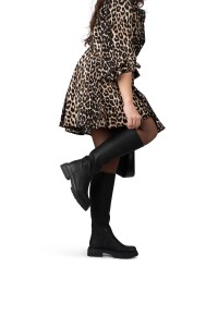 Model playfully lifting leg while wearing JAE boots with leopard dress