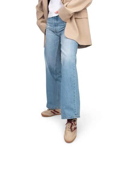 Model trägt beigefarbene POSH by Poelman Sneaker mit bordeauxroten Details zur Jeans.