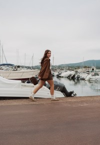 Vrouw loopt bij haven in beige loafers van PS Poelman met jas en rok