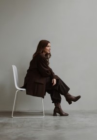 Vrouw zittend op een witte stoel, gestyled in een monochrome outfit met de donkerbruine leren DUA enkellaars