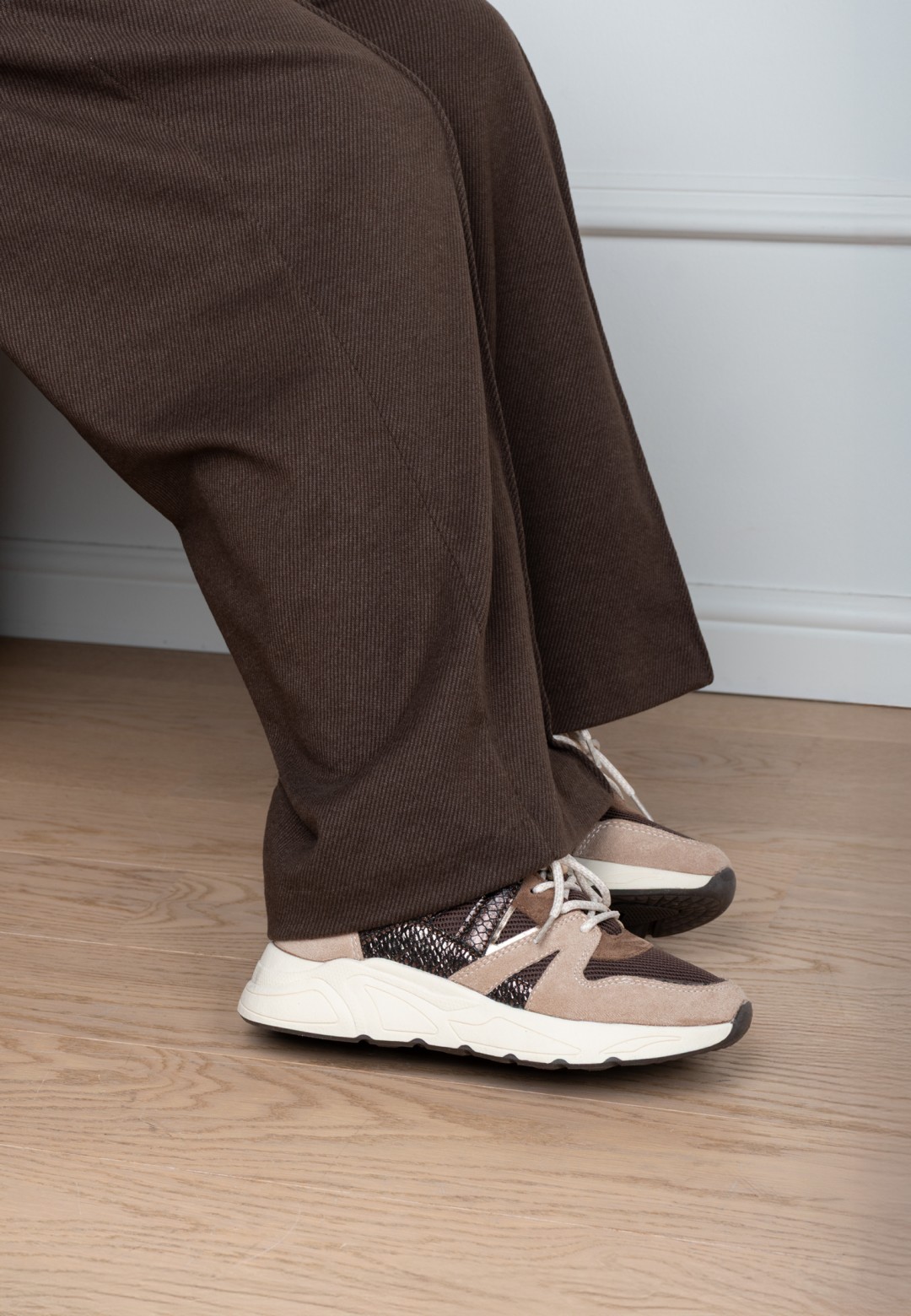 Close-up of the CAROCEL sneaker worn by model in brown trousers