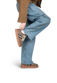 Model tilt voet op en toont LILLY sneaker met plateauzool, zijaanzicht