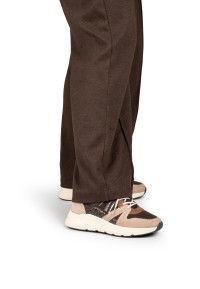 Model walking in CAROCEL sneakers by POSH by Poelman with brown wide-leg trousers, side view