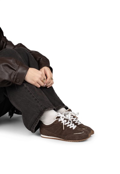 “Persoon zittend met donkere jeans en bruine suède sneakers met witte veters”