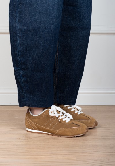 Close-up van lichtbruine sneakers gedragen onder een donkere jeans