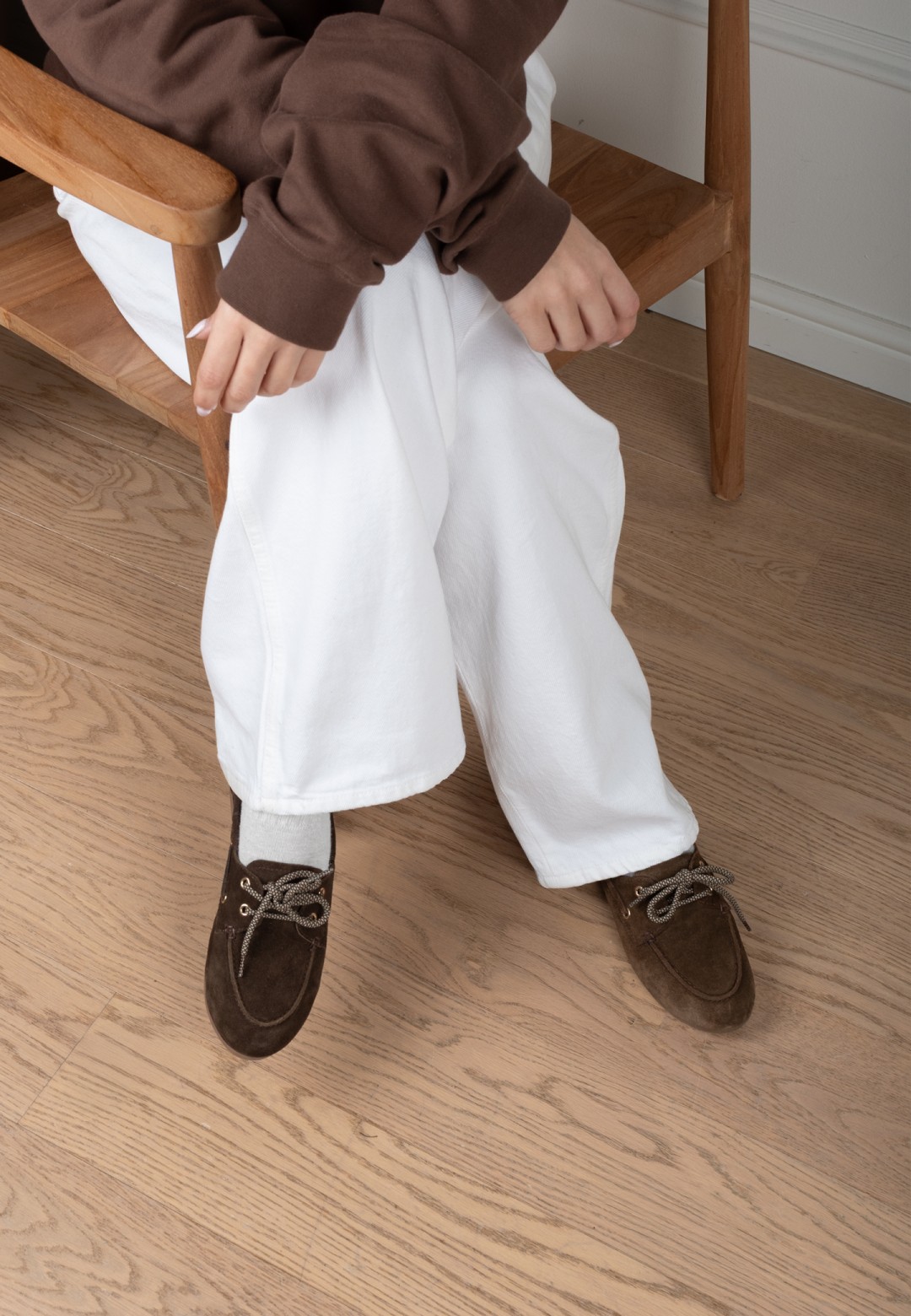 Brown suede loafers worn with white trousers, sitting pose