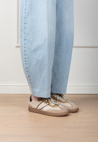 Model wearing HABOOB Skye beige sneakers with gold accents – front view