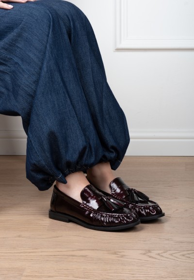 Model draagt rode POSH by Poelman RHODE loafers van lakleer met bitdetail, gecombineerd met een lichtblauwe jeans.