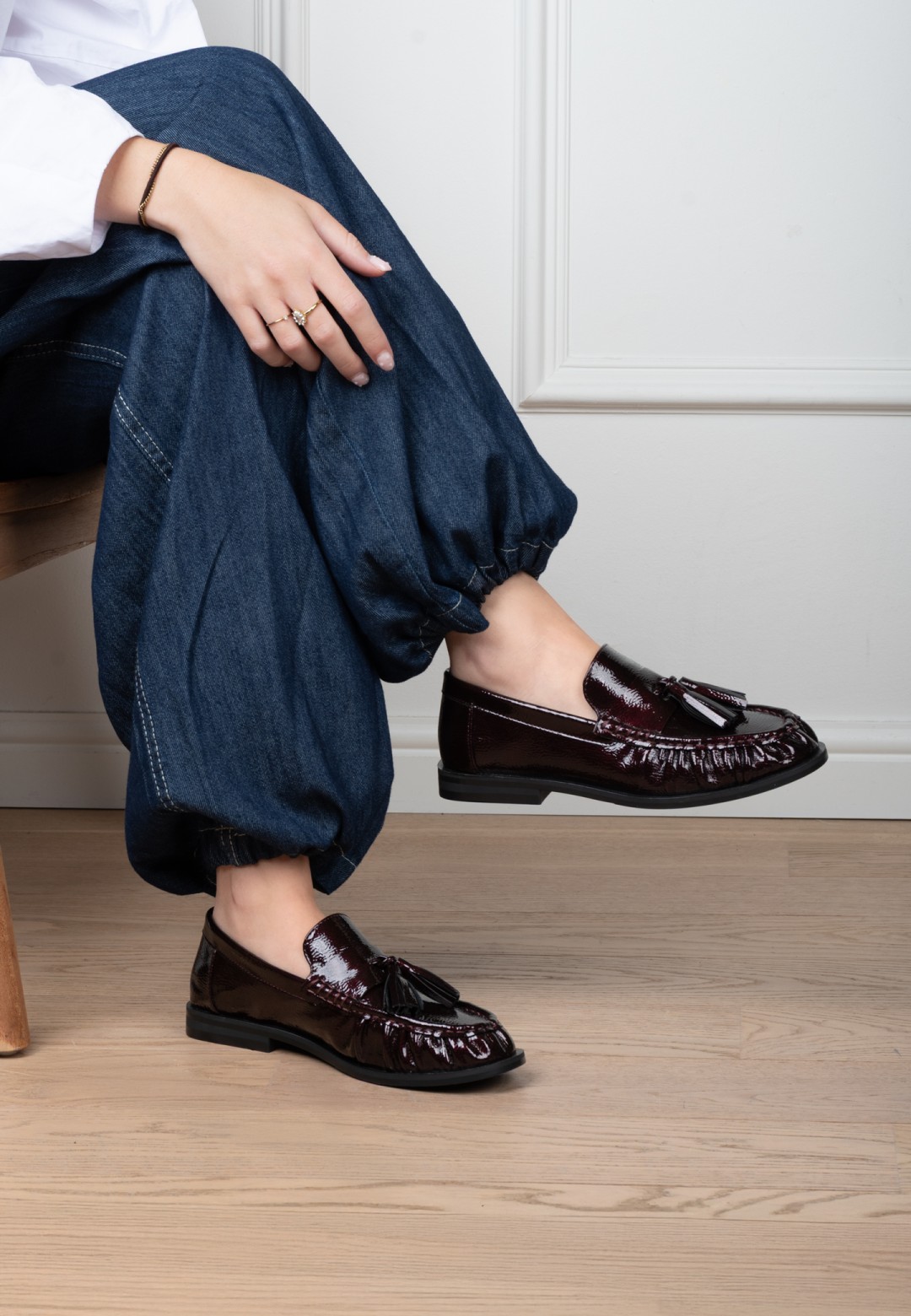 Zijaanzicht van een model dat rode POSH by Poelman RHODE loafers van lakleer draagt onder een  jeans.