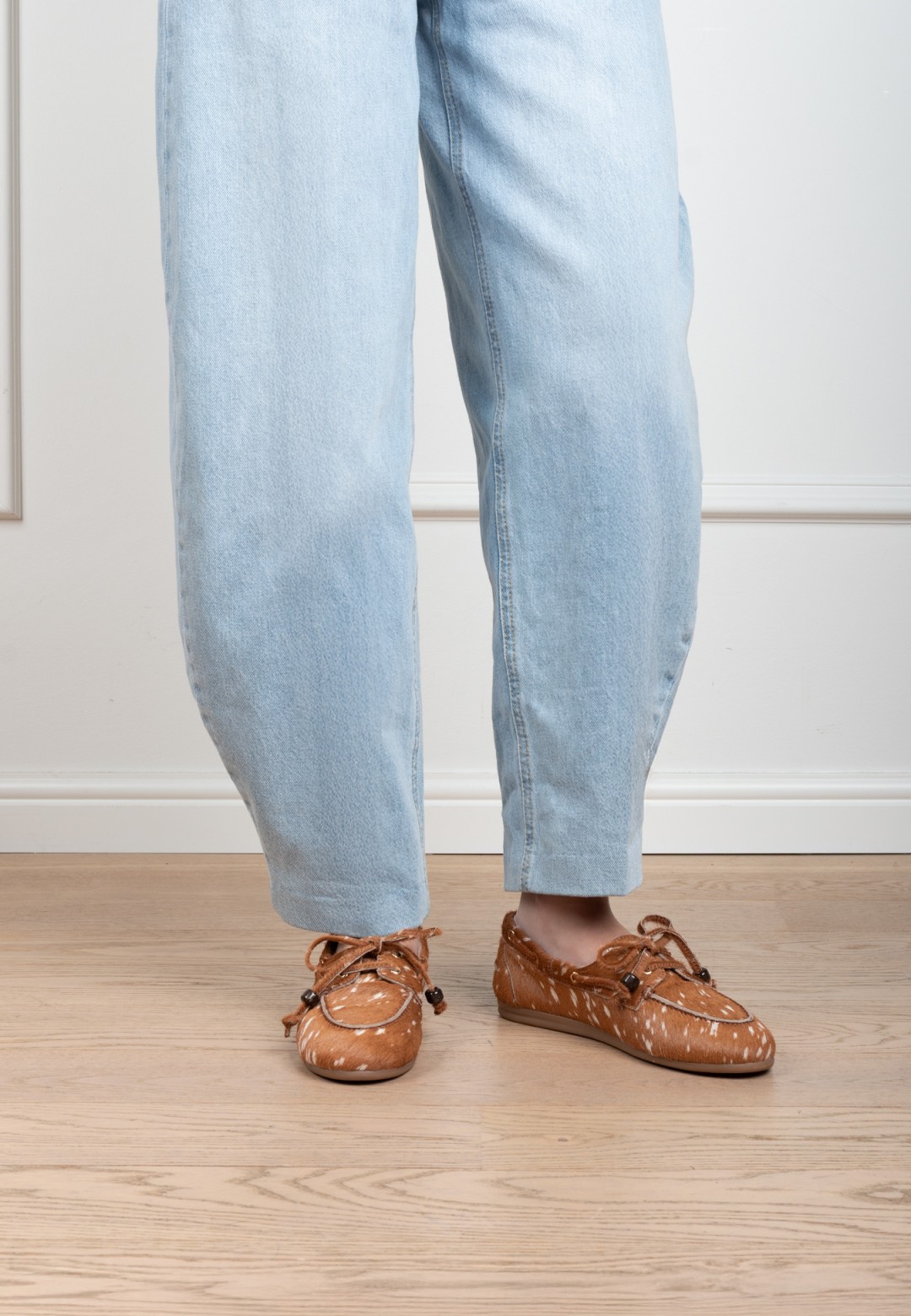 Model wearing cognac Poelman MIRA suede loafers with braided lace detail, paired with light blue jeans.