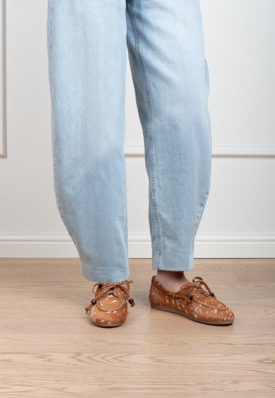 Model wearing cognac Poelman MIRA suede loafers with braided lace detail, paired with light blue jeans.
