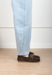Zijaanzicht van een model dat Poelman Sira loafers in donkerbruin suède met studs draagt onder een lichtblauwe jeans.
