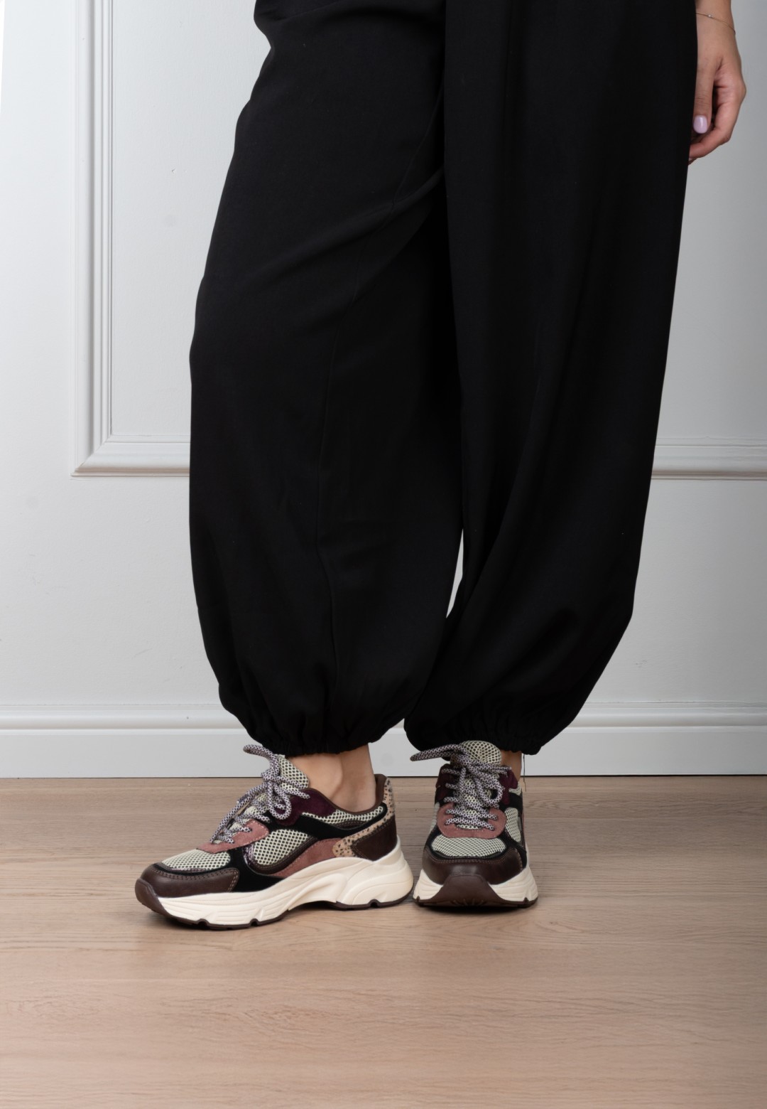 Model draagt POSH By Poelman Angy bordeaux sneakers met dierenprint en zwarte broek – vooraanzicht