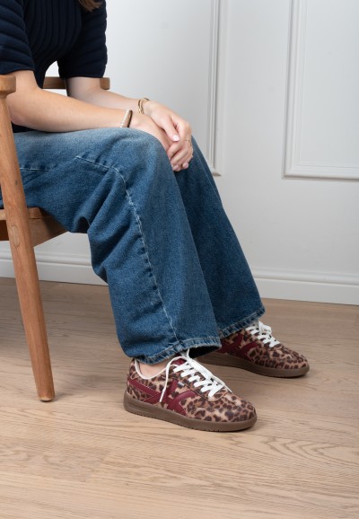 Model draagt POSH By Poelman Megan sneakers met luipaardprint en blauwe jeans – zittend
