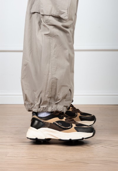 Model trägt POSH By Poelman Angy schwarz-beige Sneaker mit beiger Hose – Seitenansicht