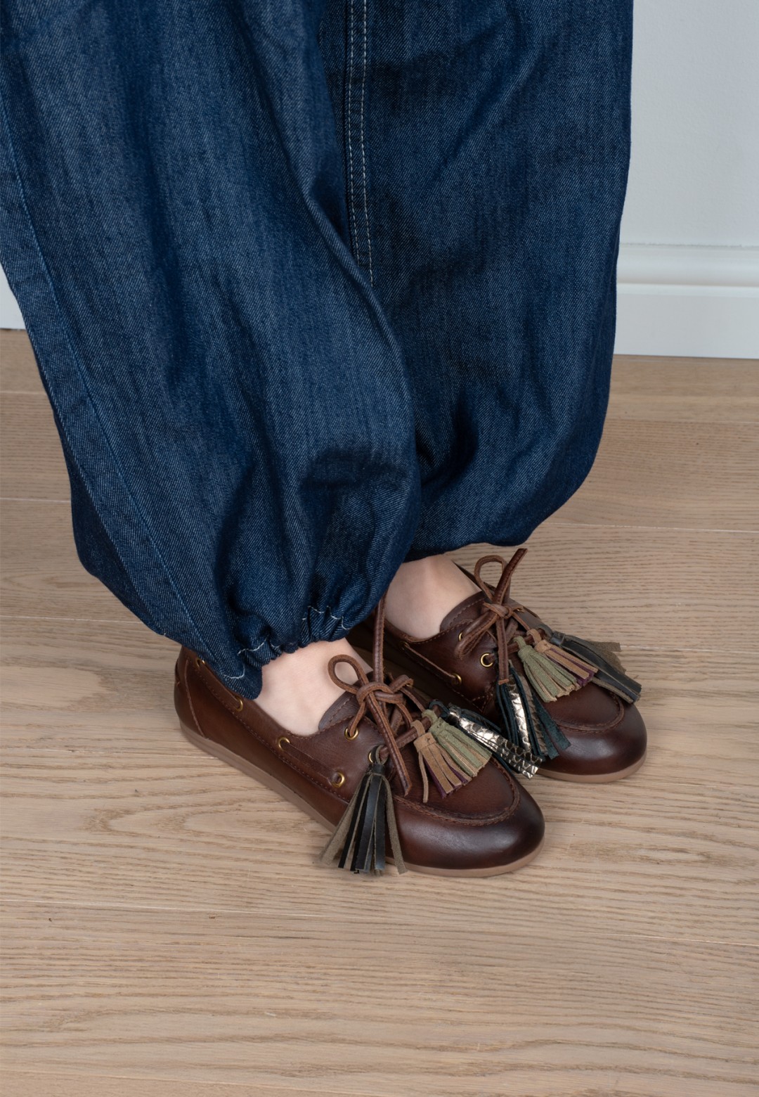Model wearing Poelman Vita brown leather loafers with tassels and wide-leg jeans – close-up