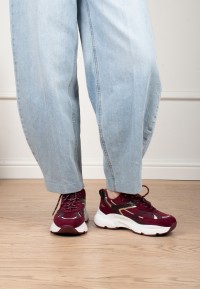 Model trägt POSH By Poelman Ayoki bordeauxfarbene Sneaker mit hellblauer Jeans – Vorderansicht