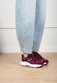 Model wearing POSH By Poelman Ayoki burgundy sneakers with light blue jeans – side view