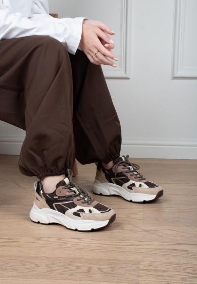 Model trägt POSH By Poelman Ayoki Sneaker in Beige, Braun und Schwarz mit brauner Hose – Vorderansicht