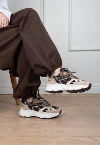 Model wearing POSH By Poelman Ayoki beige, brown and black sneakers with brown trousers – side view