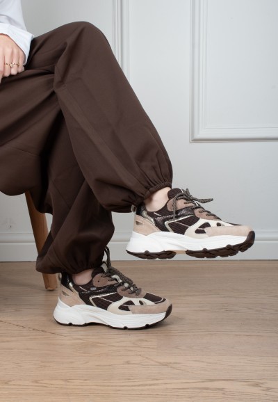 Model draagt POSH By Poelman Ayoki beige, bruine en zwarte sneakers met bruine broek – zijaanzicht
