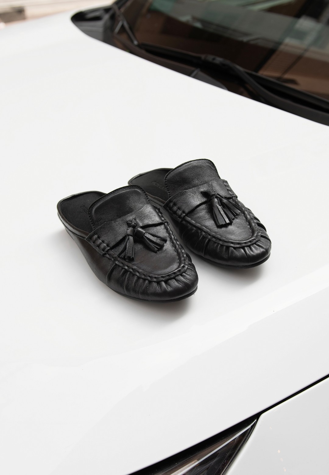 POSH by Poelman LOTTIE black loafers with buckle details on a white car