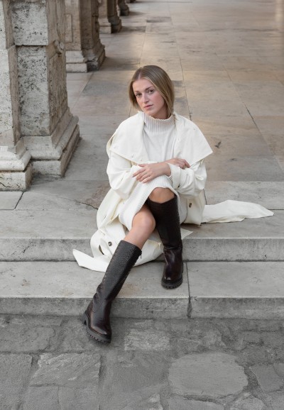 Model trägt dunkelbraune HABOOB LUNA Lederstiefel zu einem cremefarbenen Outfit auf einer Treppe