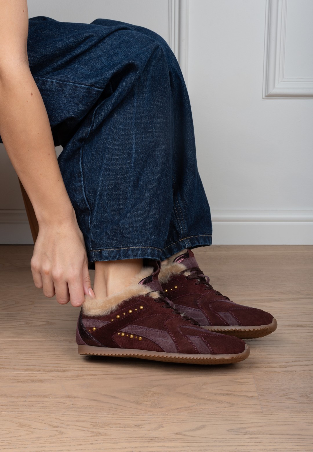 Lifestyle detail: HABOOB TAMARA dames sneaker in bordeauxrood suède met goudkleurige studs, gedragen met jeans